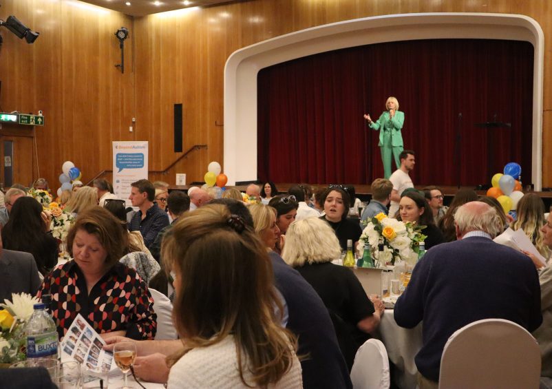 Room of people sat at tables with woman standing on stage