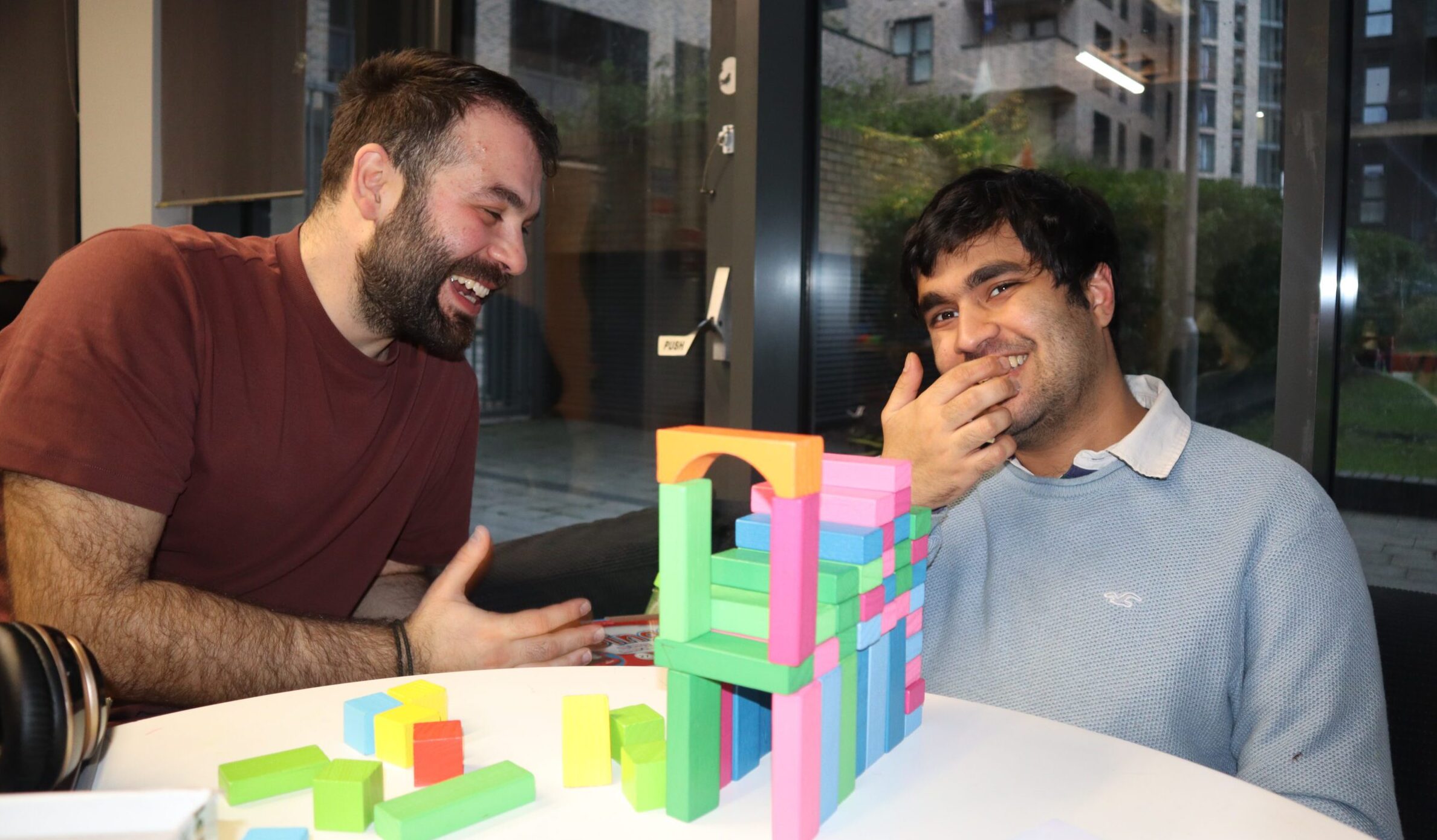 Student and staff member sat at table smiling with tower blocks